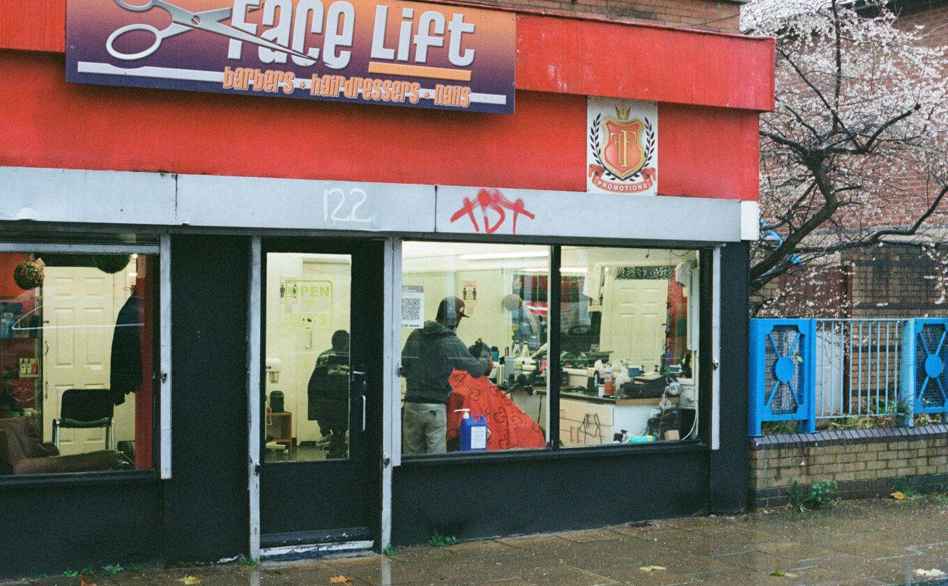 A barbershop with large windows and a red sign with the words Face Lift.