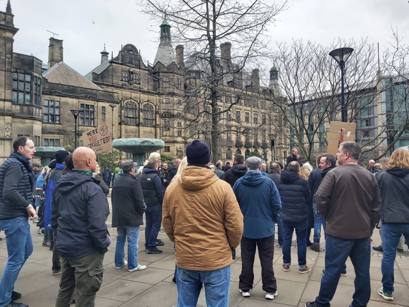 A group of mostly men stand near the Peace Gardens