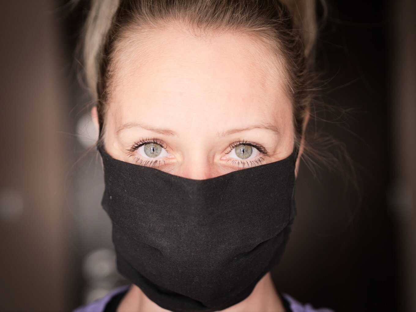 A woman looking into the camera wearing a black face mask