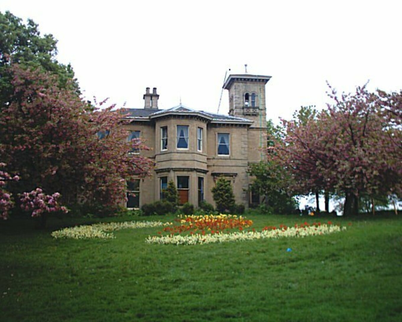 A large house amid trees and behind a neat lawn.