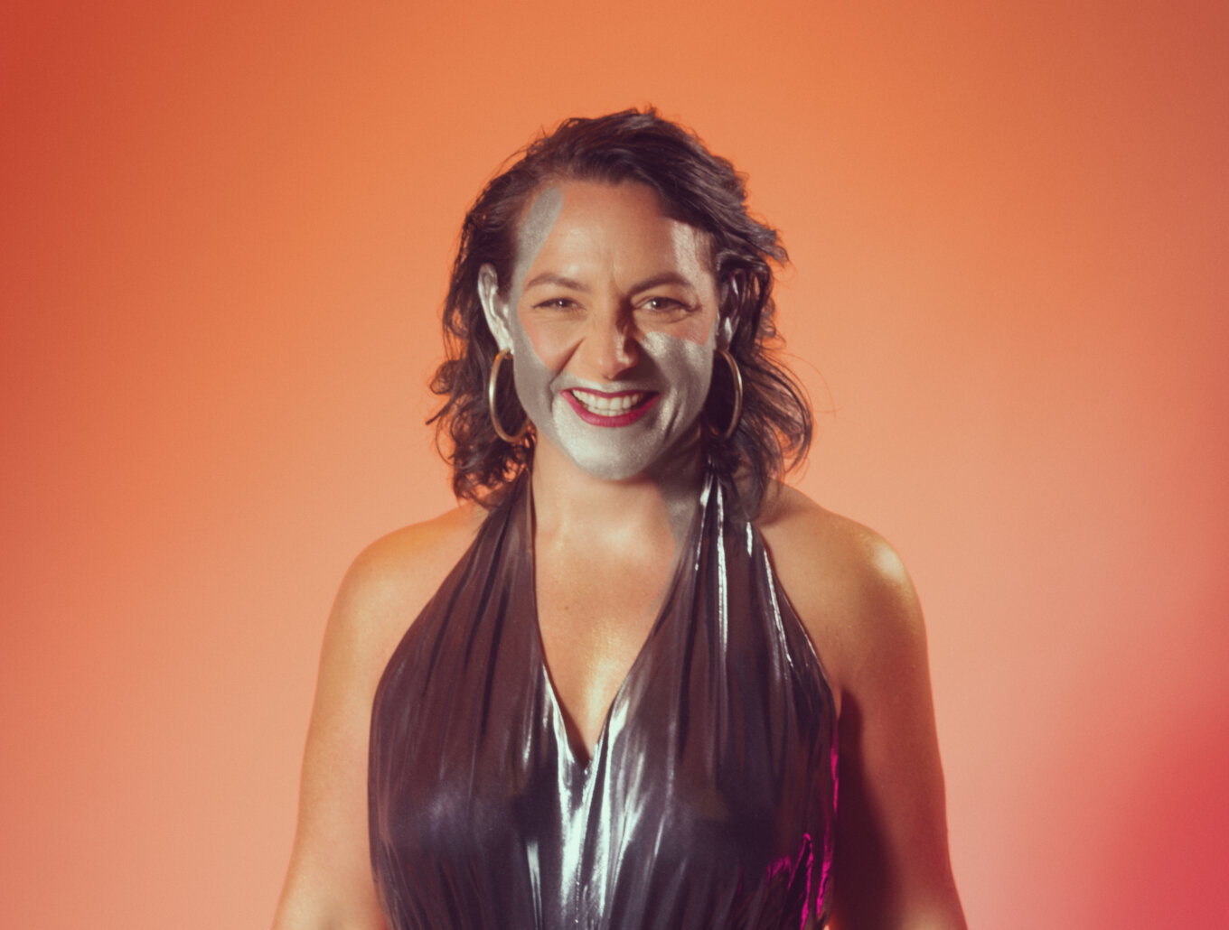 A smiling woman has metallic paint across her face.