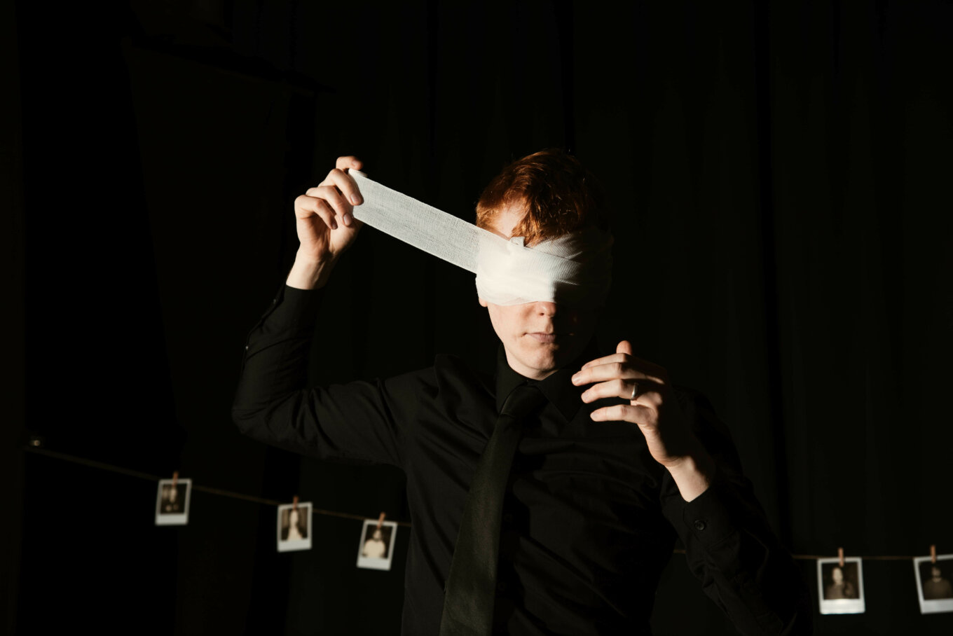 A person wraps a bandage around their eyes on a dark stage