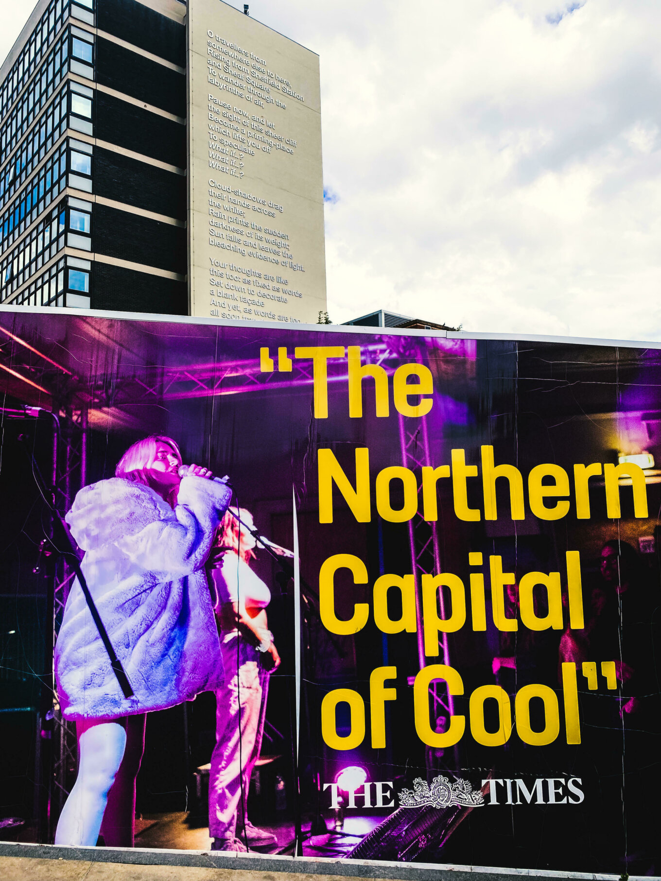 A display saying The Northern Capital of Cool in front of a tall building with a poem on the side