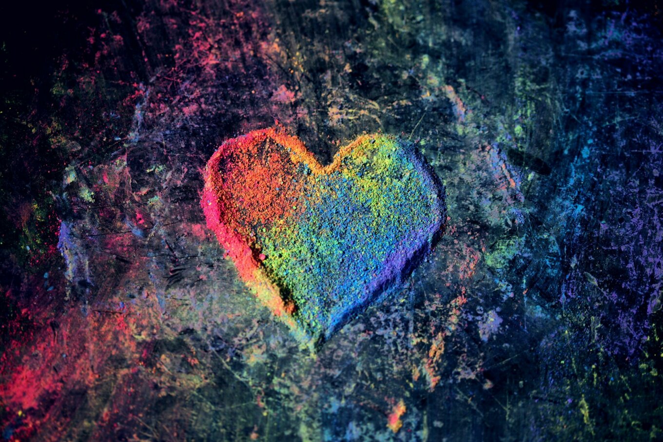 A heart in rainbow colours made out of chalk dust on a dark background.