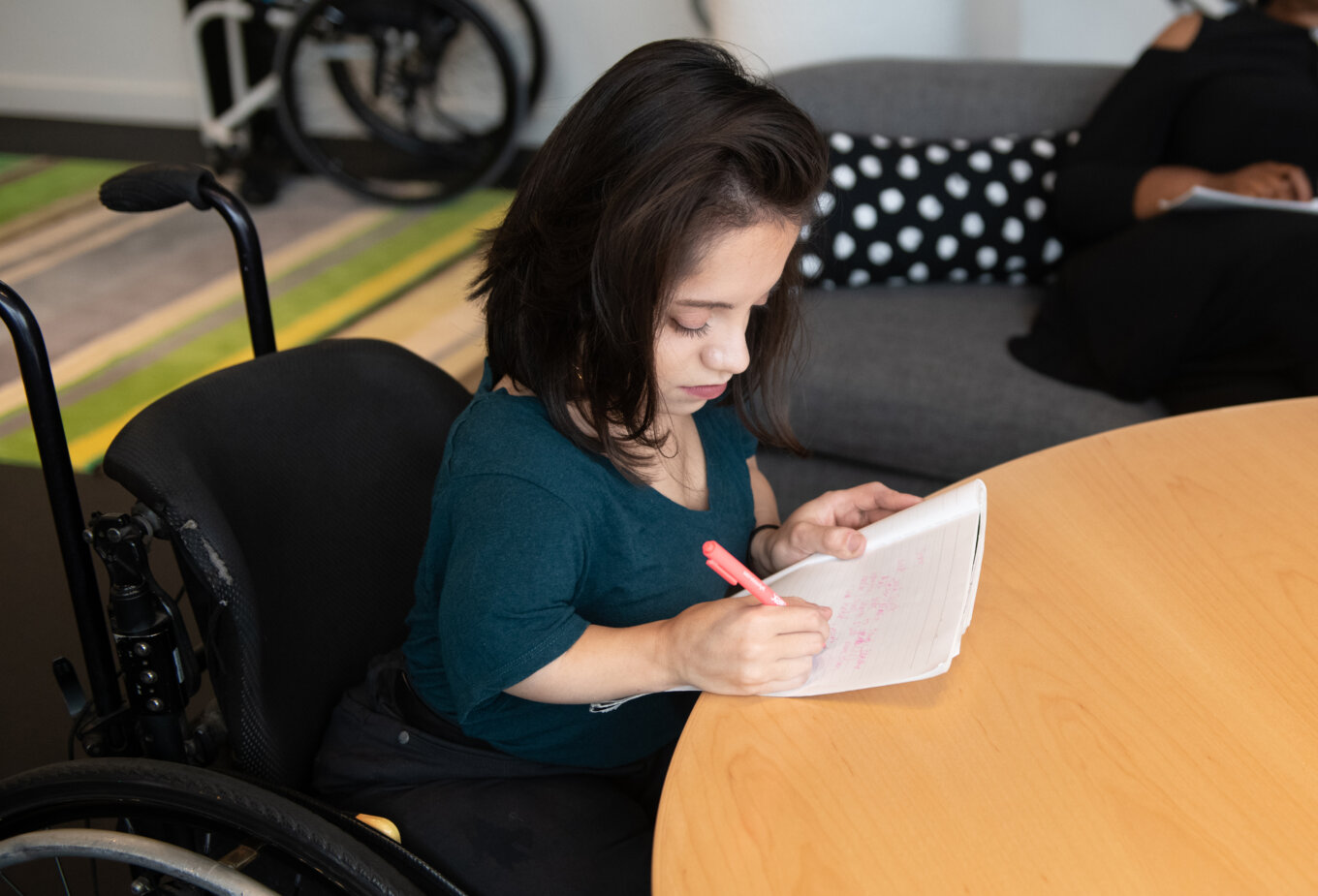 A South Asian person in her wheelchair writes by hand