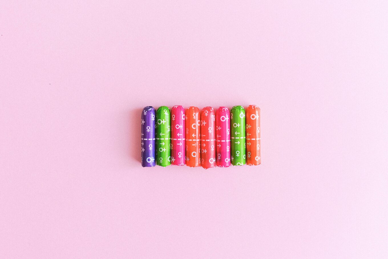 A row of different coloured tampons on a pink background.