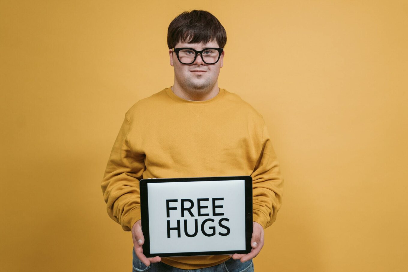 A man in a yellow jumper holds up a sign that says FREE HUGS
