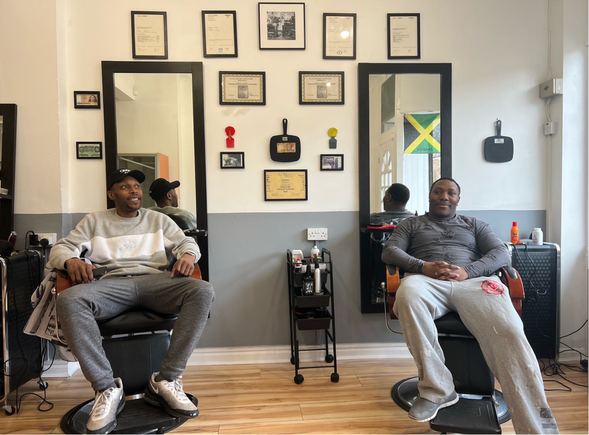 Two Black men in barbershop chairs in front of mirrors.