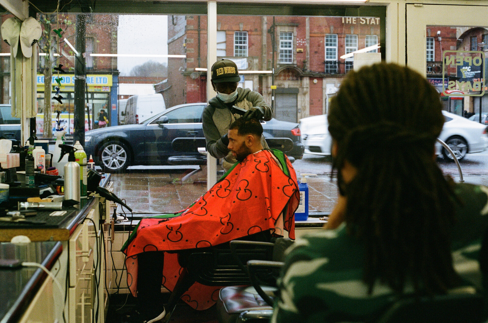 A man wearing a red clothes protector having his hair cut.