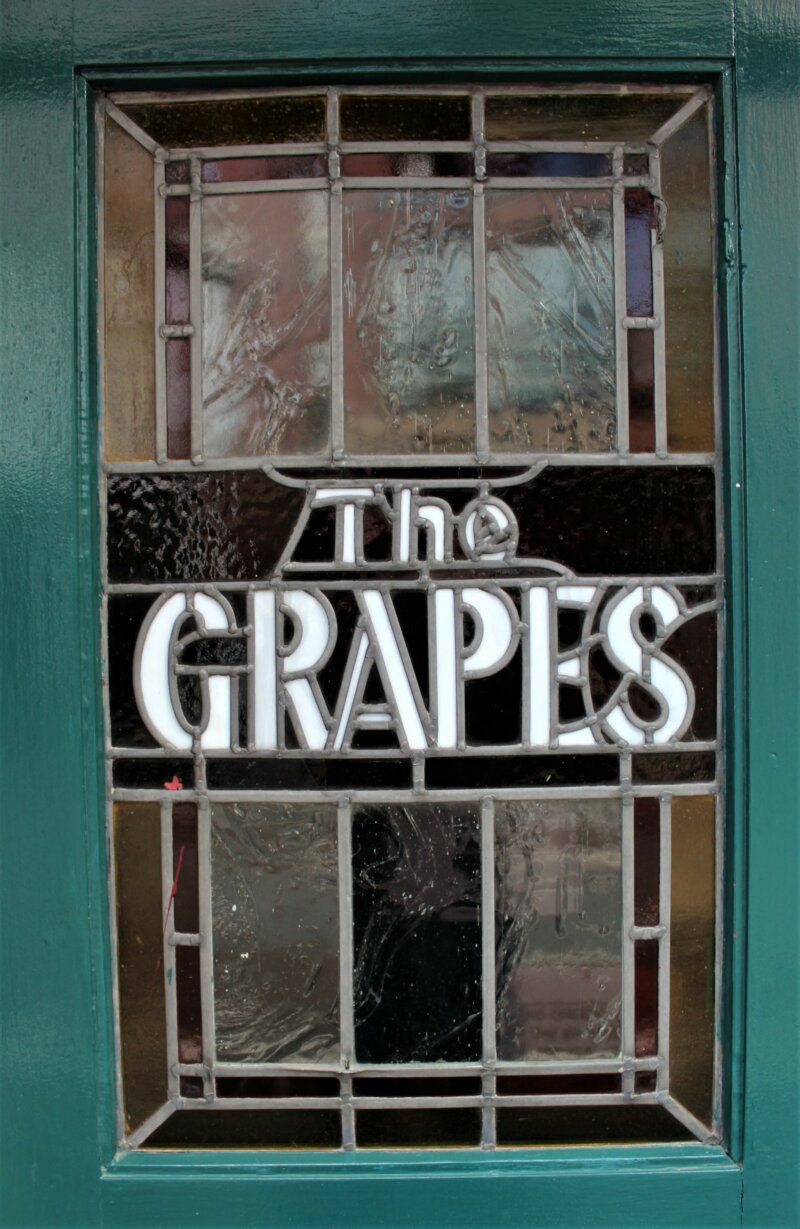 A green door with a glass feature that reads The Grapes