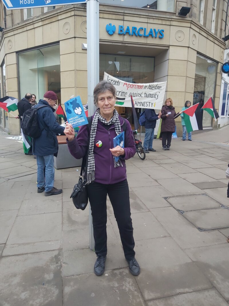 A woman standing in front of Barclays Bank with a leaflet