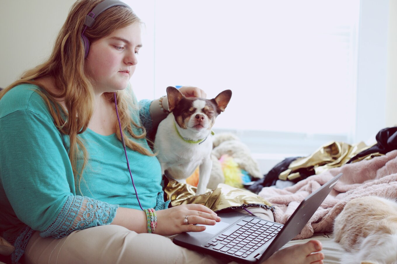 A woman sitting beside her dog at home using a laptop.